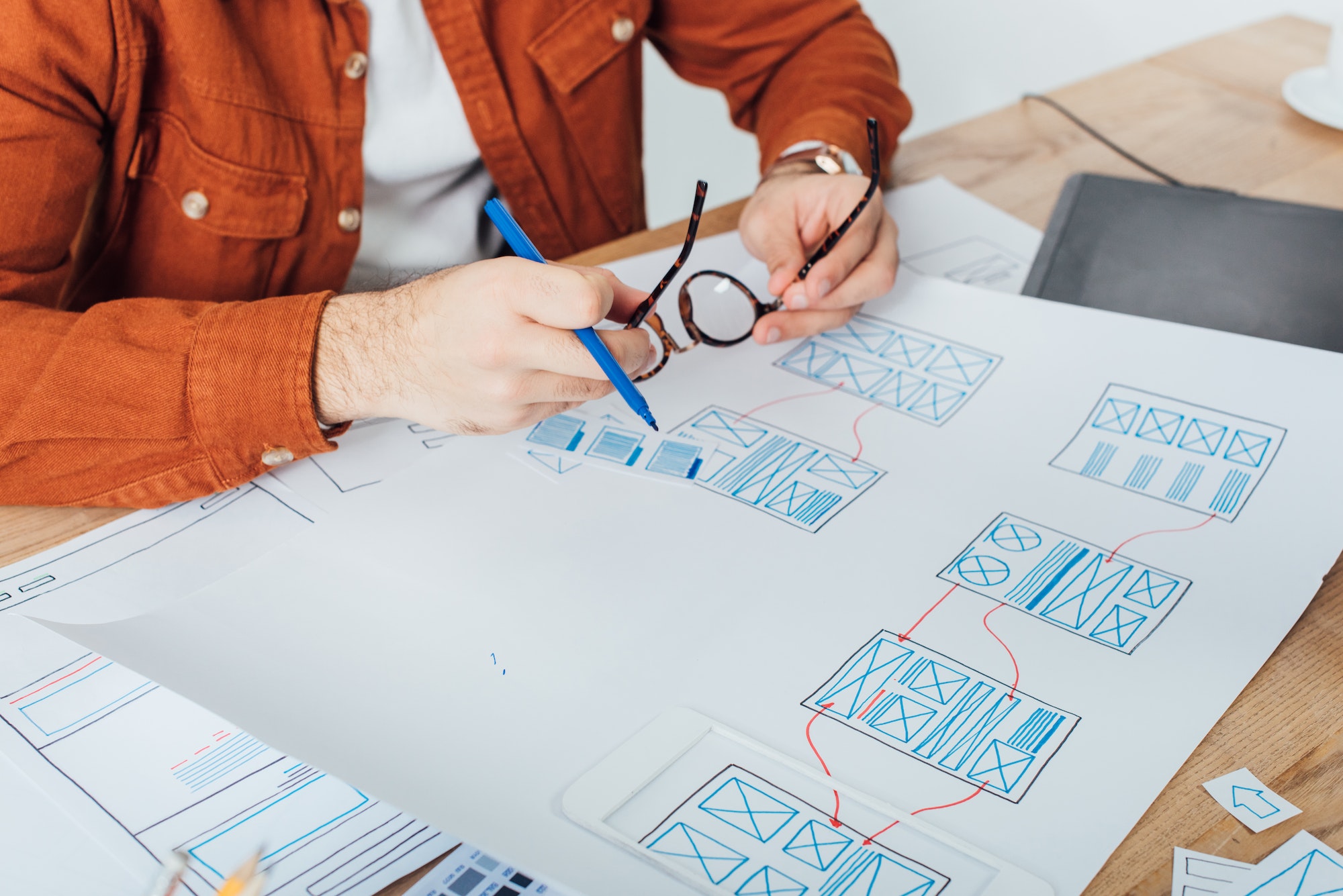 cropped-view-of-designer-holding-eyeglasses-and-marker-near-templates-of-user-experience-design-on.jpg